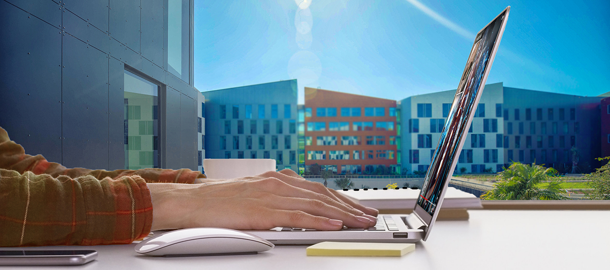 UM CARTA PhD Research Assistantships, student hands on laptop with window view of University of Miami Student Housing Village